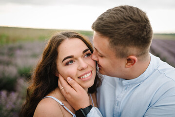 Fototapeta premium Loving couple kissing at sunset. Couple walks and enjoys floral glade and summer nature. France, Provence. Family hugging in purple lavender field of flowers. Honeymoon trip. Man and woman traveling.