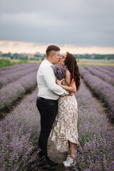 Loving couple kissing and holding bouquet of lavender flowers at sunset. Couple walks and enjoys floral glade, summer nature. France, Provence. Family hugging in purple lavender field. Honeymoon trip.