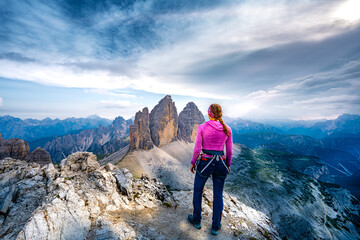Fototapeta premium Young athletic woman enjoys summit view on Tre Cime from Paternkofel in the evening. Tre Cime, Dolomites, South Tirol, Italy, Europe.