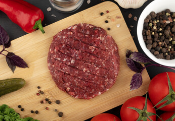 Raw hamburger cutlets on wooden cutting board with vegetables and spices