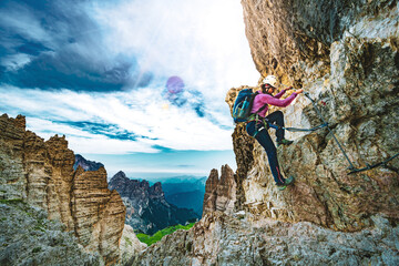 Young athletic woman hikes in via ferrata in the evening. Tre Cime, Dolomites, South Tirol, Italy,...