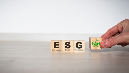 ESG concept of environmental, social and governance. Sustainable corporation development. Hand flips wooden cubes with target setting to ESG icon with other ESG icons on bright background.Copy space.