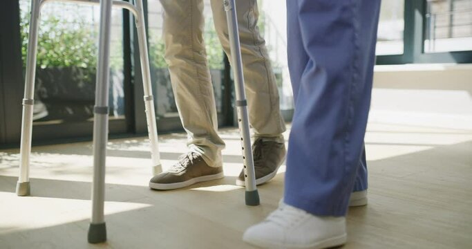 Nurse, man and feet with walker for help on floor, house and support for patient in closeup. Caregiver woman, mobility exercise and helping hand for elderly person with disability in nursing home