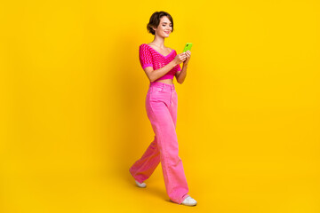 Fototapeta na wymiar Full length photo of cheerful gorgeous woman wear pink knit top go to empty space read message isolated on yellow color background