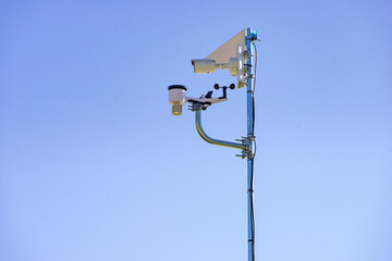 Security video camera and wind indicator against sky.