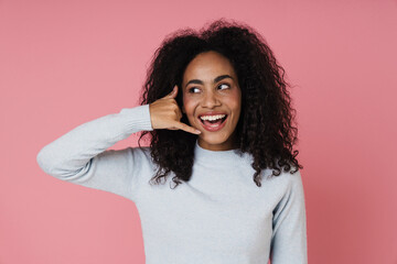 Cheerful african woman making call gesture while standing isolated over pink wall