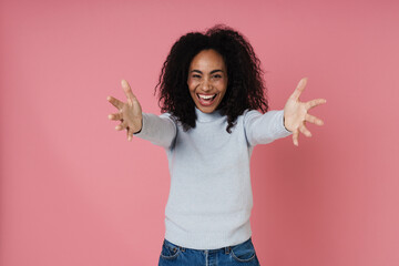 Friendly african woman stretching her arms for hug while standing isolated over pink wall