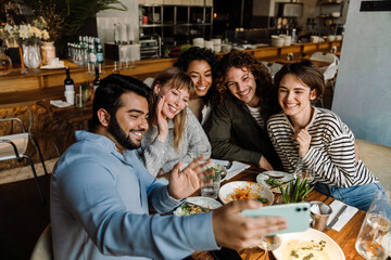 Group of joyful friends taking selfie while dining in restaurant