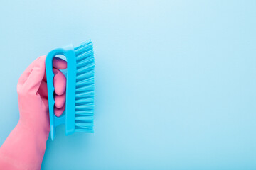 Cleaner hand in pink rubber protective glove holding and showing new cleaning brush on light blue table background. Pastel color. Closeup. Empty place for text. Top down view.