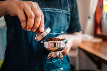 Close-up of hand barista or coffee maker holding portafilter and coffee tamper making an espresso coffee.