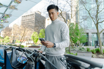 Serious asian man holding mobile phone, scanning mobile app, bicycle rental on street