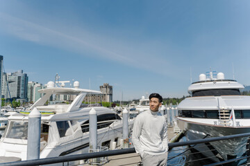 Fototapeta na wymiar Portrait of asian rich man standing near expensive yachts, looking away outdoors
