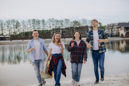 Joyful friends, holding refreshing summer alcoholic beverages, make their way back from the lake after a relaxing time. A girl carries a basket filled with fresh fruits, a man holding a bag of drinks.
