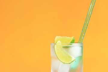 Lemonade with ice and lime on a bright orange background. Summer cocktail with cold drink. Copy space. Drink with a straw close-up