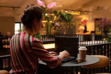 Woman freelancer working on a laptop at the table in cafe alone