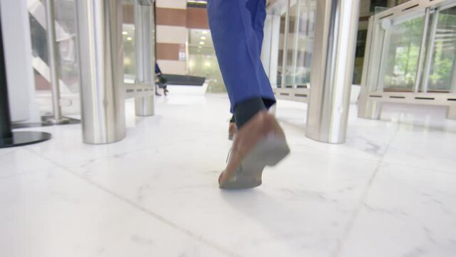 Camera follows at a low angle a smart professional executive through a building lobby to the elevator, in slow motion