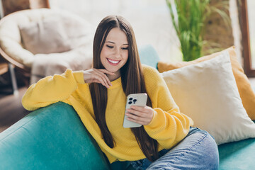 Photo of cheerful pretty girl sit comfy couch toothy smile use smart phone chatting free time...