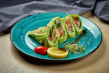 Spinach roll pancakes with salmon and cream cheese in a plate. Ukrainian crepes or mlynets, blini