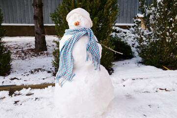 Happy snowman with carrot nose, white woolen hat and blue scarf in winter scenery. Merry christmas...