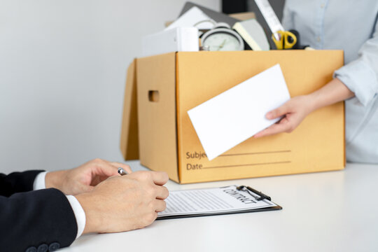 The Asian female employee holding a box containing her personal belongings, handed over her resignation letter to the supervisor, signifying the end of her chapter within the company.