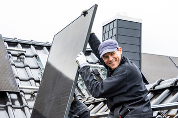 Smiling tradesman installing a solar panel on a roof of a house