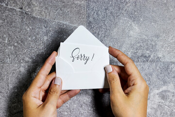 woman hand holding a white envelope with sorry concept on gray grunge background
