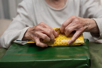 manos de mujer anciana abriendo regalos con papel amarillo