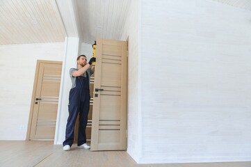 A handsome male worker is installing a new door in a house.