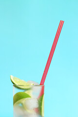 Lemonade with ice and lime on a light blue background. Summer cocktail with cold drink. copy space. Drink with a straw close-up