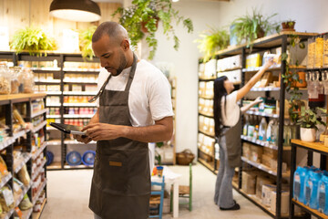 Ethnic salesman in apron standing near shelf in grocery store