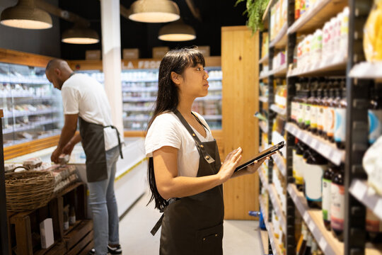 Ethnic sales staff checking tablet for grocery items in shelf