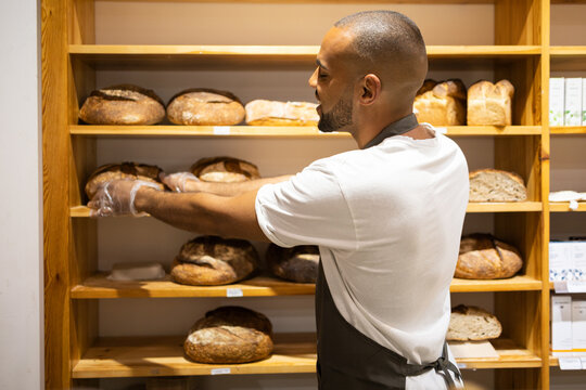 Cheerful black man with bread in bakery shop