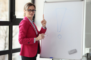 Woman in glasses stands by whiteboard with exclamation mark