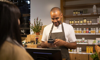 Smiling ethnic man in apron checking POS terminal