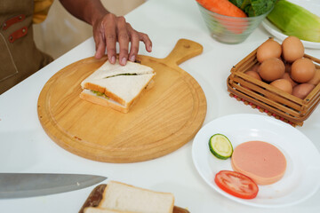 Asian hand close up Garnishing the egg sandwich After using a knife to cut a sandwich that was placed on a wooden chopping board. To prepare breakfast on the day that I have to work from home