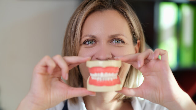 Positive dentist holds human jaws model by face in hospital