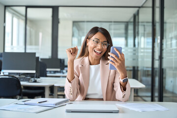 Excited young African American business woman winner executive looking at cell phone celebrating financial success, happy about professional results receiving mobile message on cellphone in office.