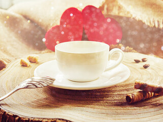White cup with coffee, on a wooden background in the morning sun. Two red hearts in the background. Valentine's Day. Selective focus.