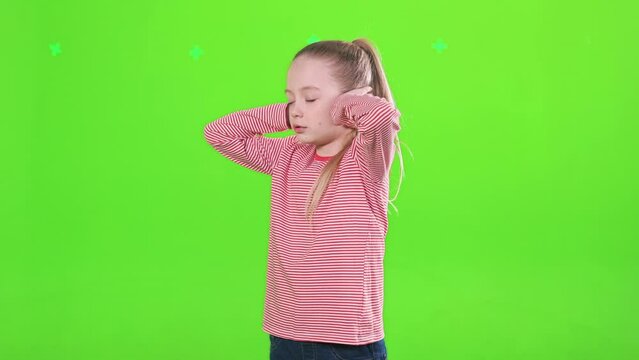 Serious little girl covering ears with hands, doesn't want to hear in studio. Side view of offended female kid with closed eyes, listening nothing, swinging, isolated on green. Concept of expression.