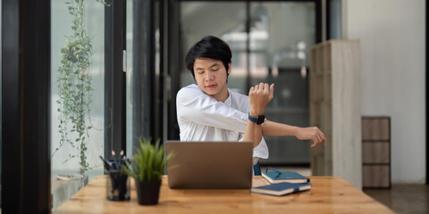 Stretching oneself asian business man with laptop in cafe. tried from work, stretch oneself
