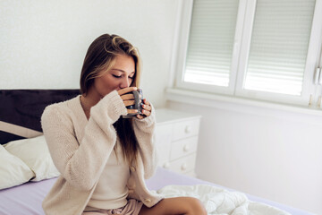 Woman drinking coffee while sitting on the bed in the morning. Woman holding a cup of coffee in her bedroom. sitting on bed and smiling.