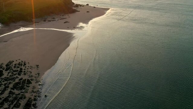 Tilting drone shot revealing Bigbury beach at golden sunrise