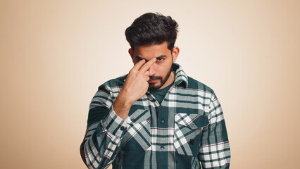 Fototapeta premium I am watching you. Young confident indian man pointing at his eyes and camera, show I am watching you gesture, spying on someone. Handsome bearded hindu guy isolated alone on beige studio background