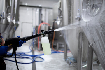 worker's hand hold a high pressure cleaner gun and put foam on equipment on the factory