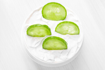 Pure white cucumber moisturizer in a white jar.   White towel. Green Cucumber.