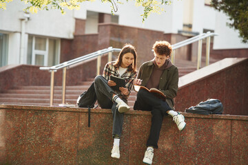 Sitting together. Man and woman students are outdoors near university