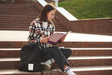 Young female student is sitting on the stairs of university
