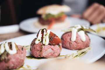 Three raw meat balls snack with white sauce, tomatoes on a plate 