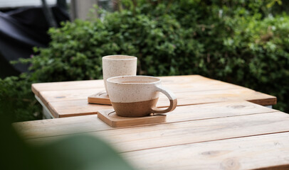 Two cups of coffee and tea on a wooden table, green trees around 