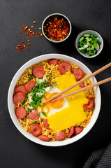 Ramen Noodles with Sausages, Egg, Melted Cheese and Scallion, Microwave Shin Ramyeon or Ramyun on Dark Background